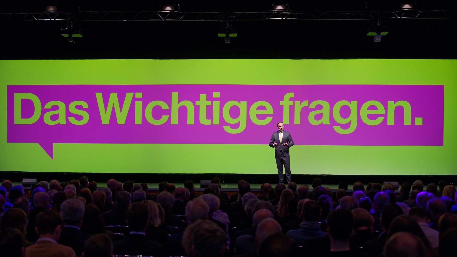 Christian Lindner steht vor Publikum auf einer Bühne, im Hintergrund ein Banner mit der Aufschrift "Das Wichtige fragen". Christian Lindner steht vor Publikum auf einer Bühne, im Hintergrund ein Banner mit der Aufschrift "Das Wichtige fragen".