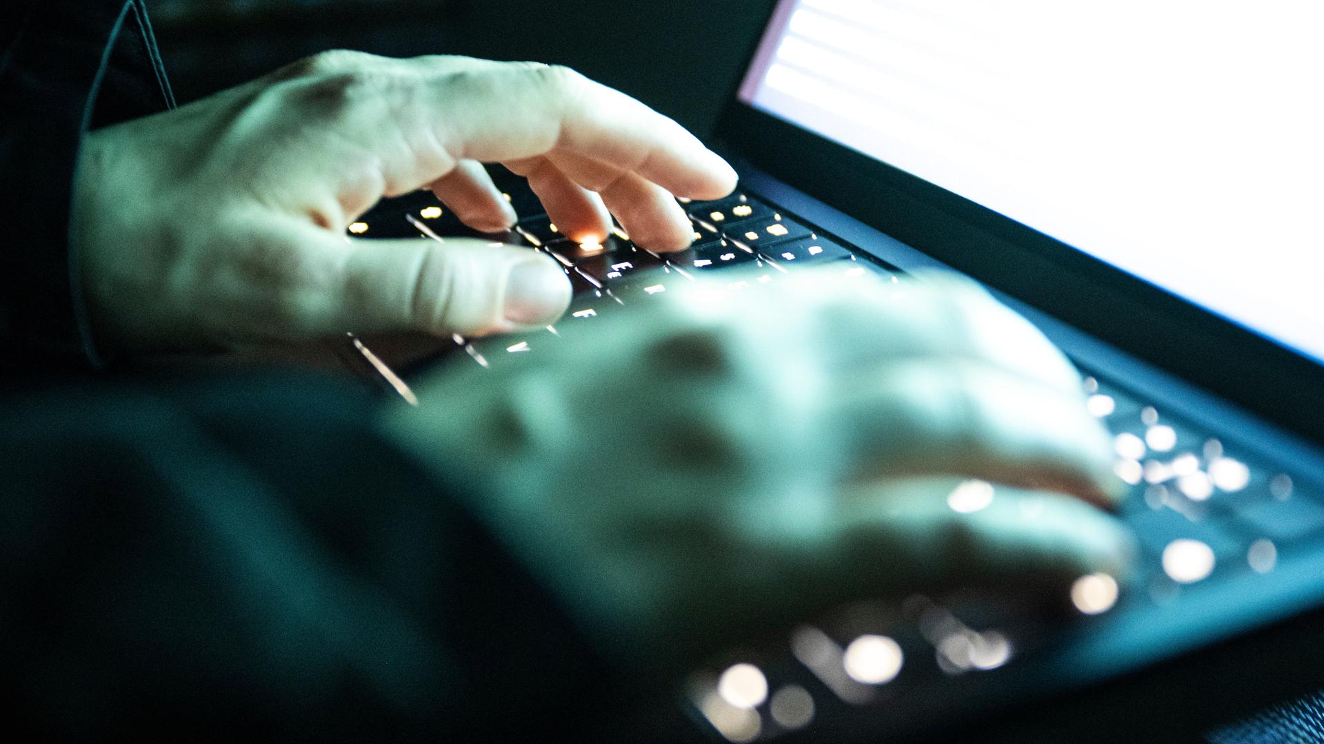 Eine Person tippt mit den Fingern auf einer beleuchteten Laptop-Tastatur.