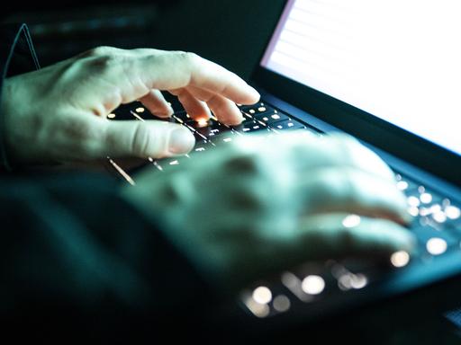 Eine Person tippt mit den Fingern auf einer beleuchteten Laptop-Tastatur.