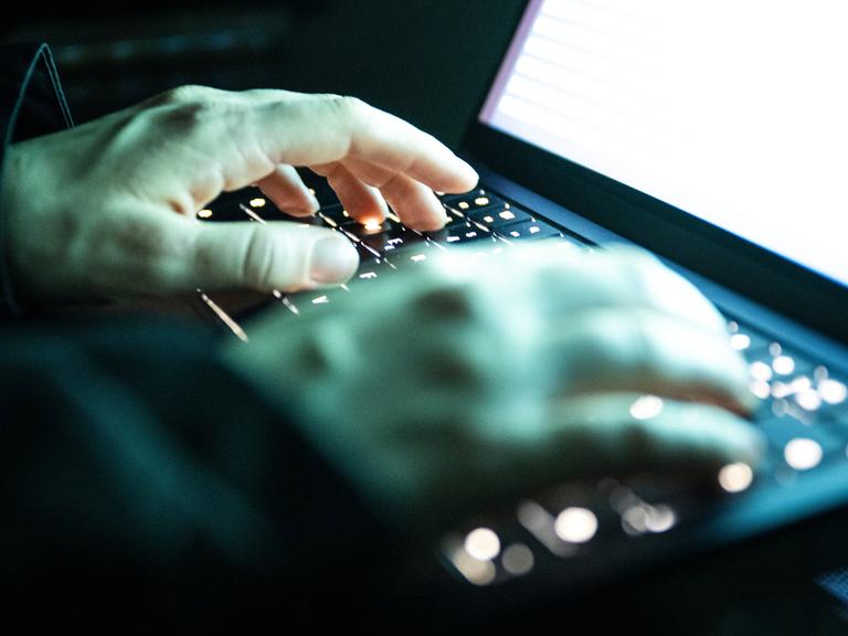 Eine Person tippt mit den Fingern auf einer beleuchteten Laptop-Tastatur.