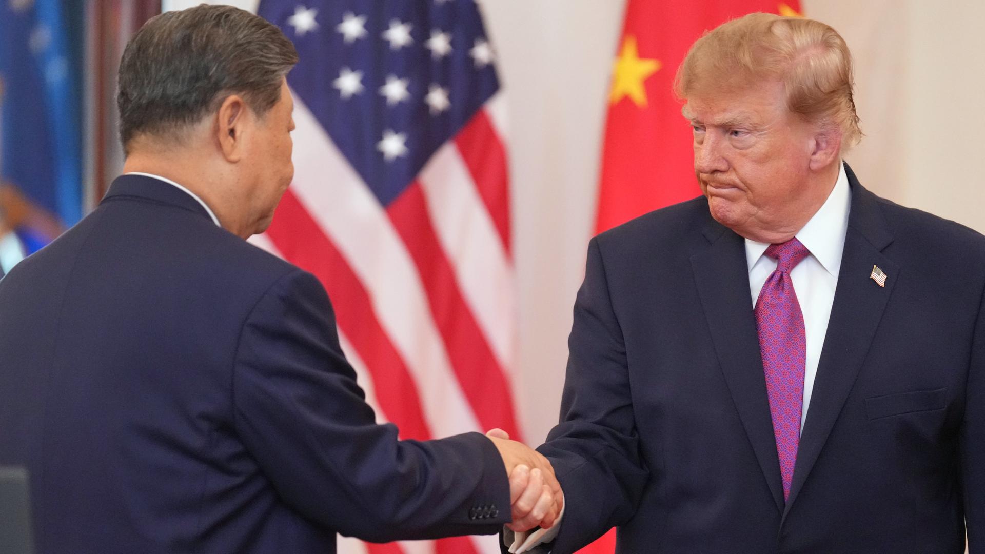 US-Präsident Trump und Chinas Staatschef Xi geben sich die Hand. Im Hintergrund stehen die Flaggen der USA und Chinas.