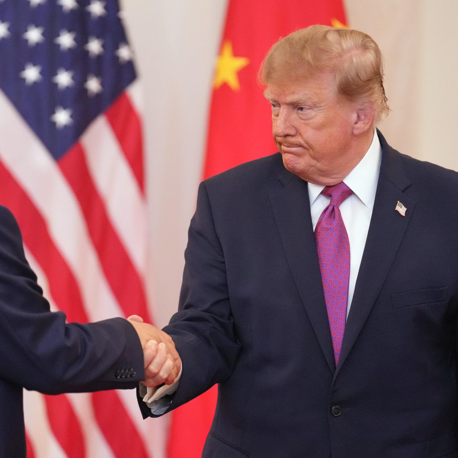 US-Präsident Trump und Chinas Staatschef Xi geben sich die Hand. Im Hintergrund stehen die Flaggen der USA und Chinas.