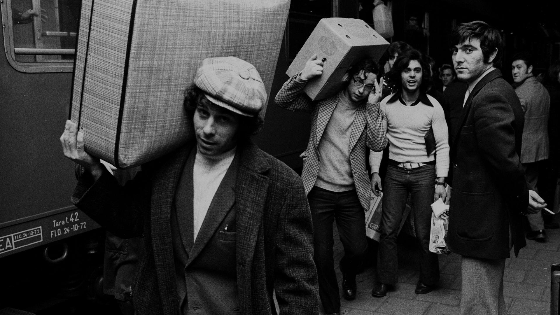 Italienische Gastarbeiter, bei VW in Wolfsburg beschäftigt, fahren in den Weihnachtsurlaub Richtung Italien - hier am 16.12.1972 vom Wolfsburger Bahnhof. Ein Mann mit Locken und Schirmmütze trägt seinen Koffer lässig auf der Schulter.
