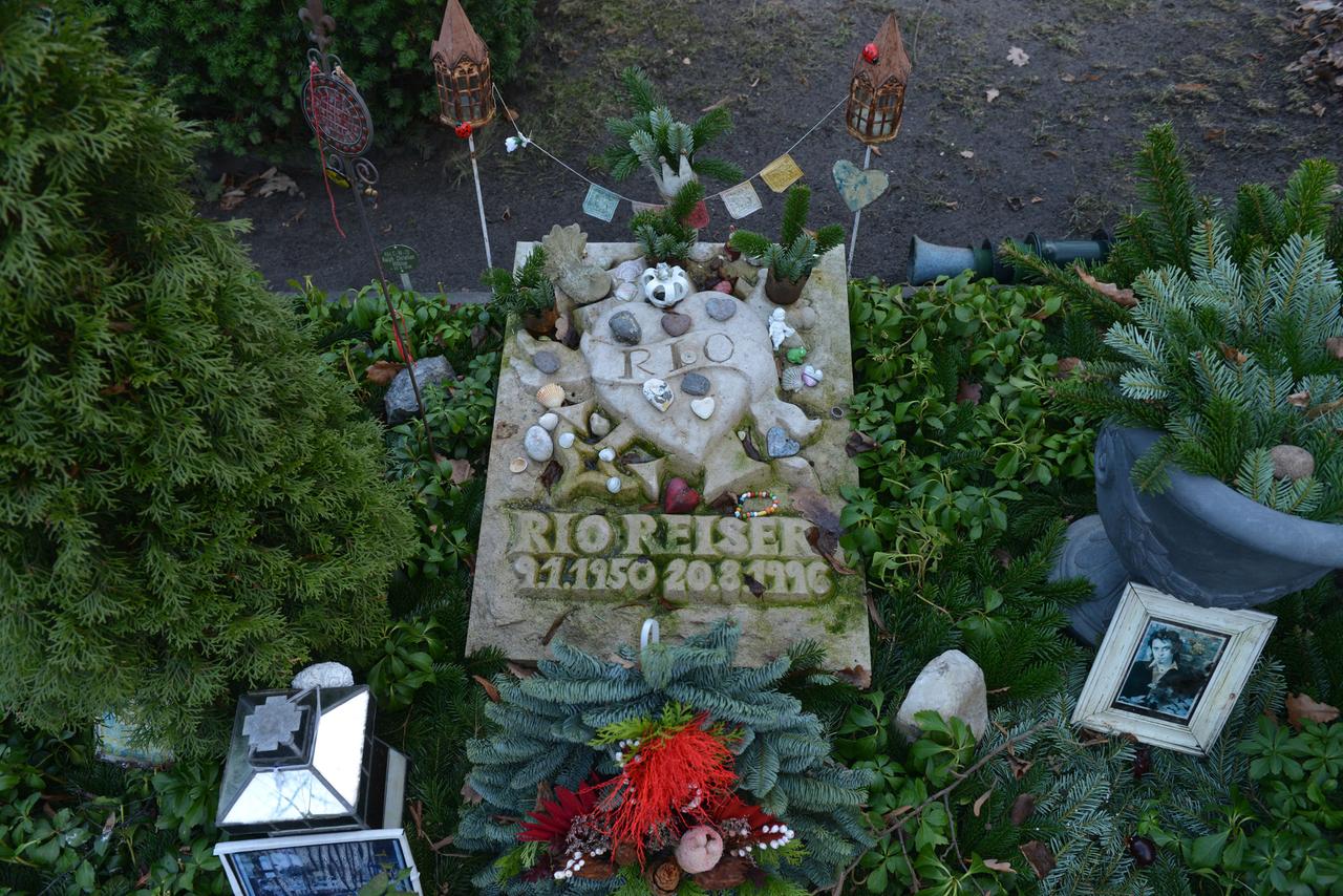 Blick auf das Grab von Sänger Rio Reiser auf dem Alten St. Matthäus-Kirchhof in Berlin-Schöneberg. Teil des Grabsteins ist ein großes Herz mit der Aufschrift „RIO“. Neben dem Grabstein ist ein Foto des Musikers zu sehen. 