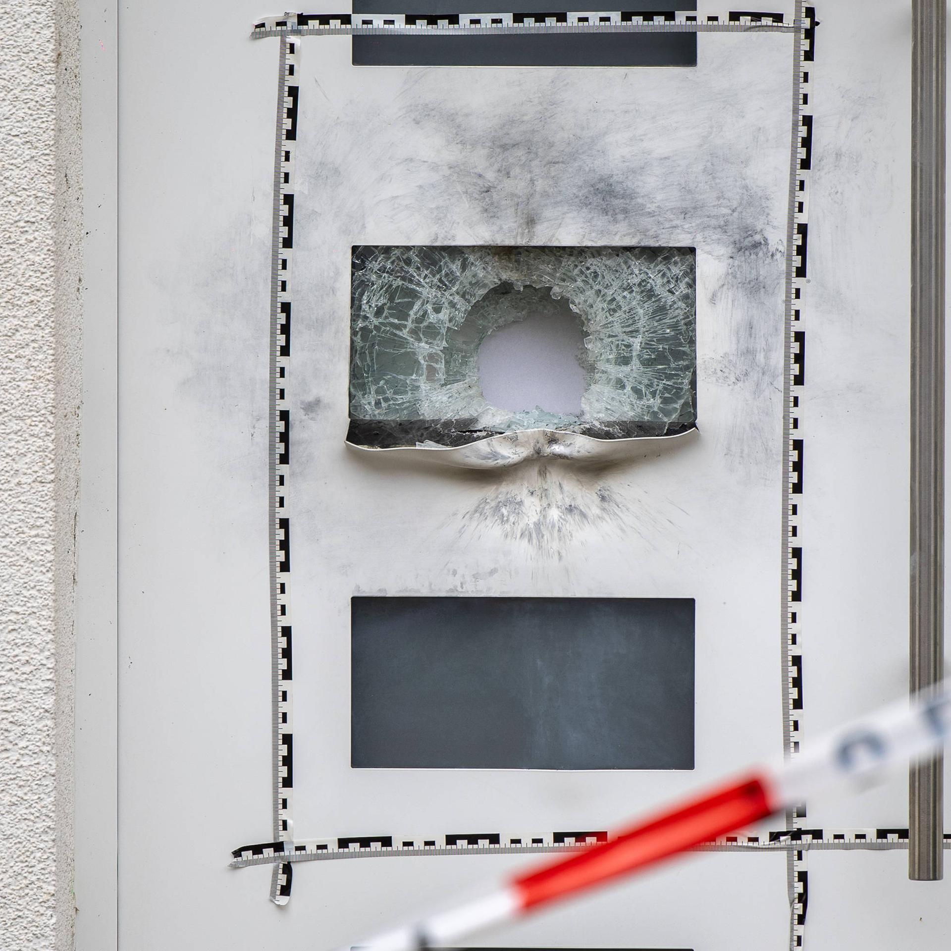 Ein Loch in der Scheibe einer Eingangstür, darum sind Rauchspuren zu erkennen.