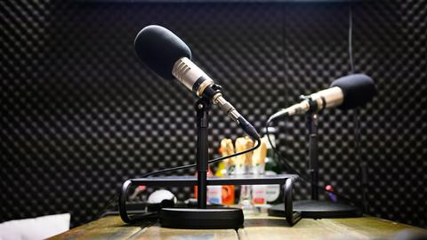 Zwei Podcast-Mikrofone stehen in einem Tonstudio auf einem Tisch.