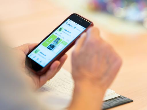 Eine Person hält ein Smartphone in der Hand, auf dessen Display die App nebenan.de geöffnet ist.