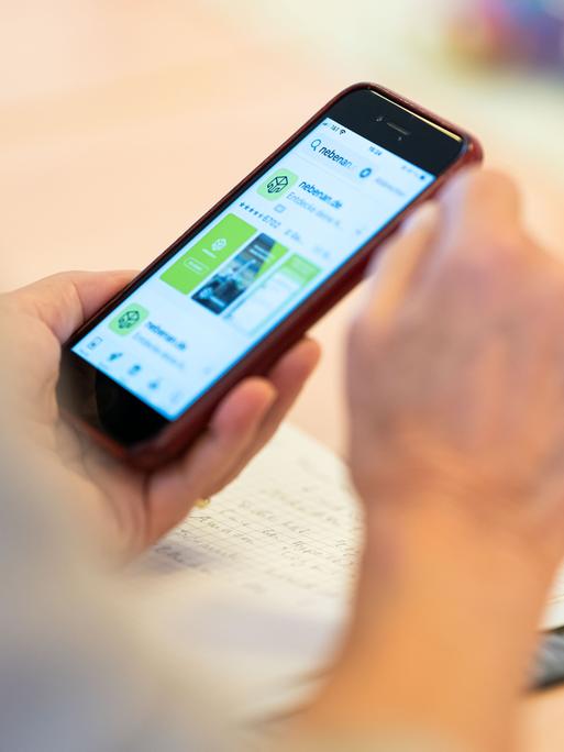 Eine Person hält ein Smartphone in der Hand, auf dessen Display die App nebenan.de geöffnet ist.