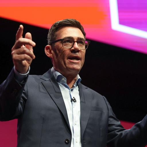 Andy Burnham steht auf einer Bühne und hält eine Rede. Dabei hat er eine entschlossene Miene und gestikuliert entschlossen mit seinen Händen.