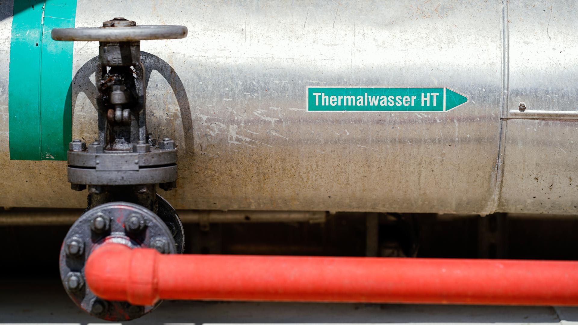 Abgebildet ist ein Teil einer technischen Anlage, bestehend aus einem dünnen roten Rohr, einem Sperrventil und einem breiten Rohr in Metalltönen. Darauf klebt ein Schild mit der Aufschrift “Thermalwasser HT”
Abgebildet ist ein Teil einer technischen Anlage, bestehend aus einem dünnen roten Rohr, einem Sperrventil und einem breiten Rohr in Metalltönen. Darauf klebt ein Schild mit der Aufschrift “Thermalwasser HT”