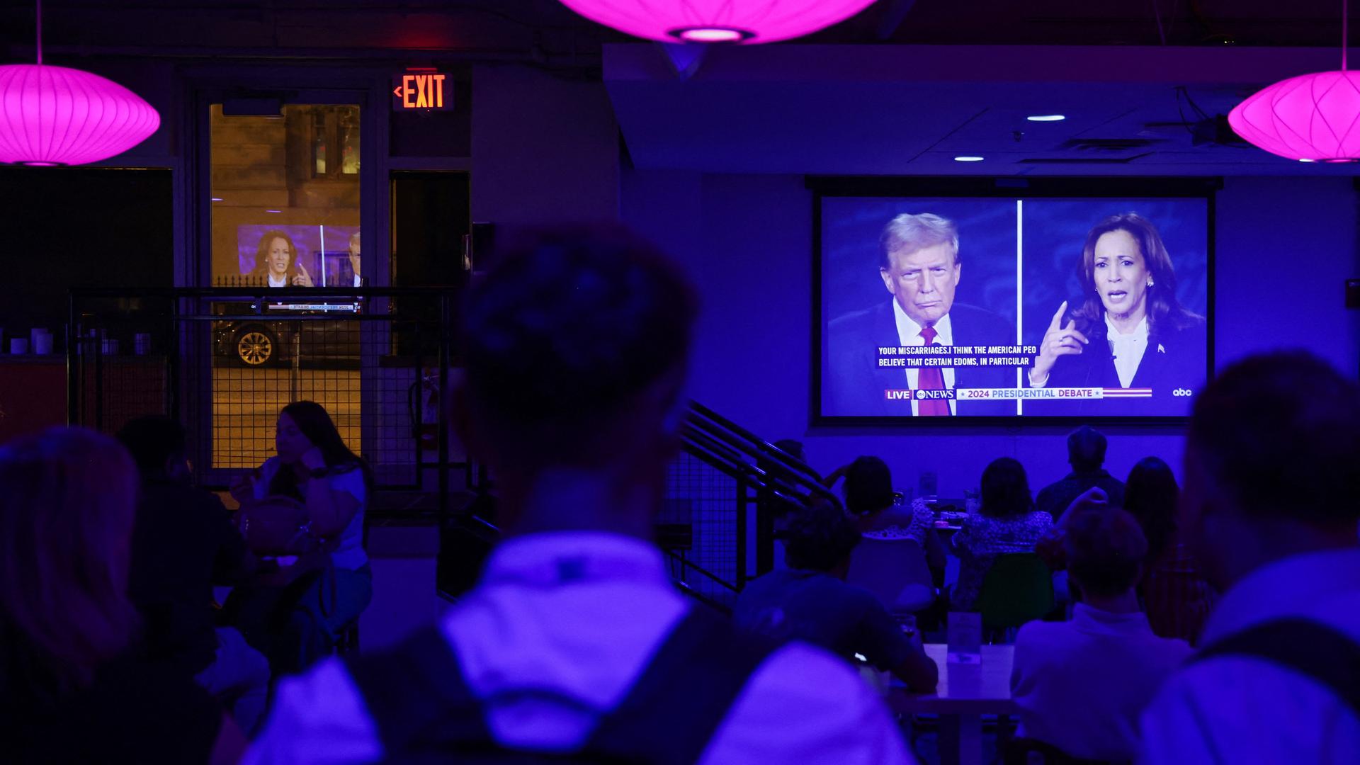 Menschen in einer Bar verfolgen auf einem großen TV-Bildschirm die Debatte zwischen Kamala Harris und Donald Trump.