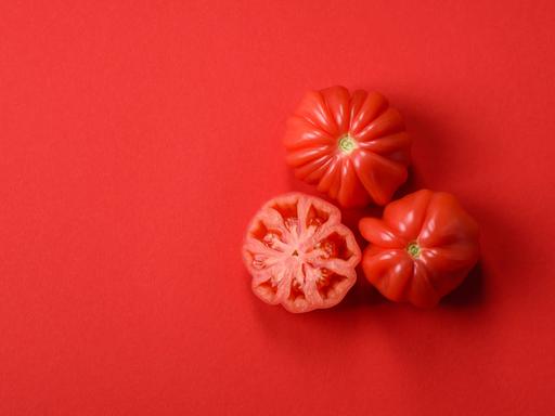 Drei aufgeschnittene Tomaten liegen auf rotem Grund