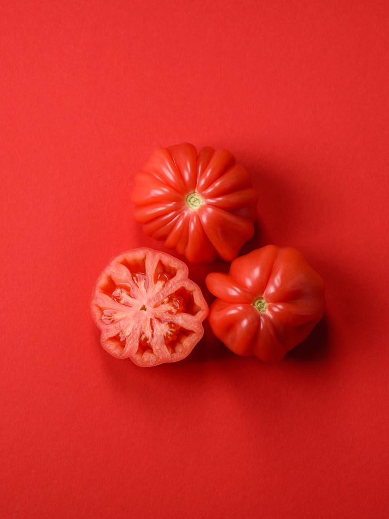 Drei aufgeschnittene Tomaten liegen auf rotem Grund