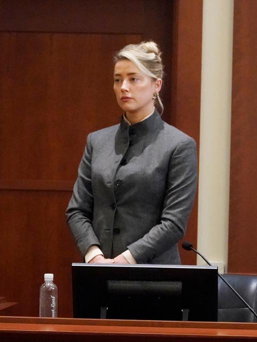Amber Heard stehend bei einer Aussage im Gerichtssaal, im Vordergrund hört ihr Ex-Ehemann Johnny Depp zu.