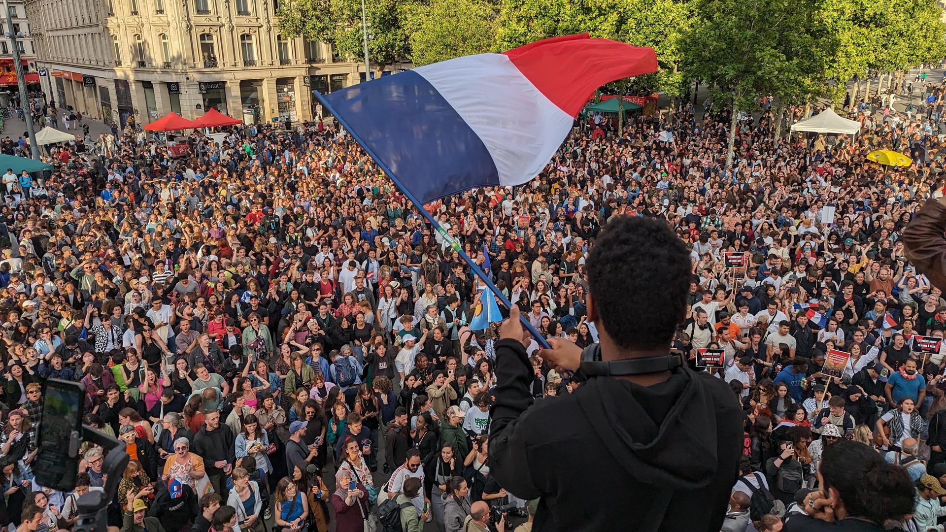 In Paris feiern tausende den Wahlsieg des Linksbündnisses bei der Stichwahl. Ein junger Mann hält eine Frankreichflagge in der Händen, 07.07.2024.