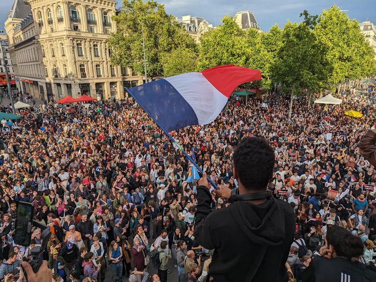 In Paris feiern tausende den Wahlsieg des Linksbündnisses bei der Stichwahl. Ein junger Mann hält eine Frankreichflagge in der Händen, 07.07.2024.