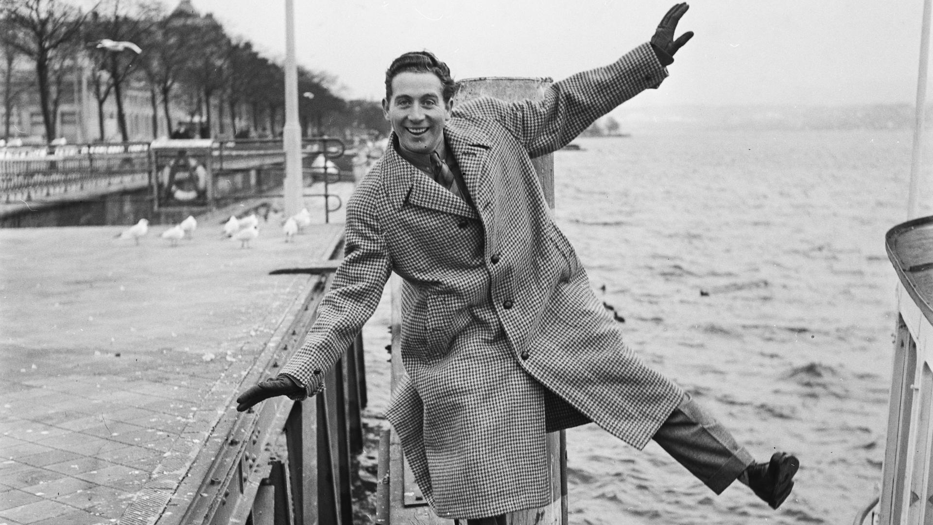 Charles Trenet posiert mit von sich gestreckten Armen und Beinen auf einem Bootssteg.