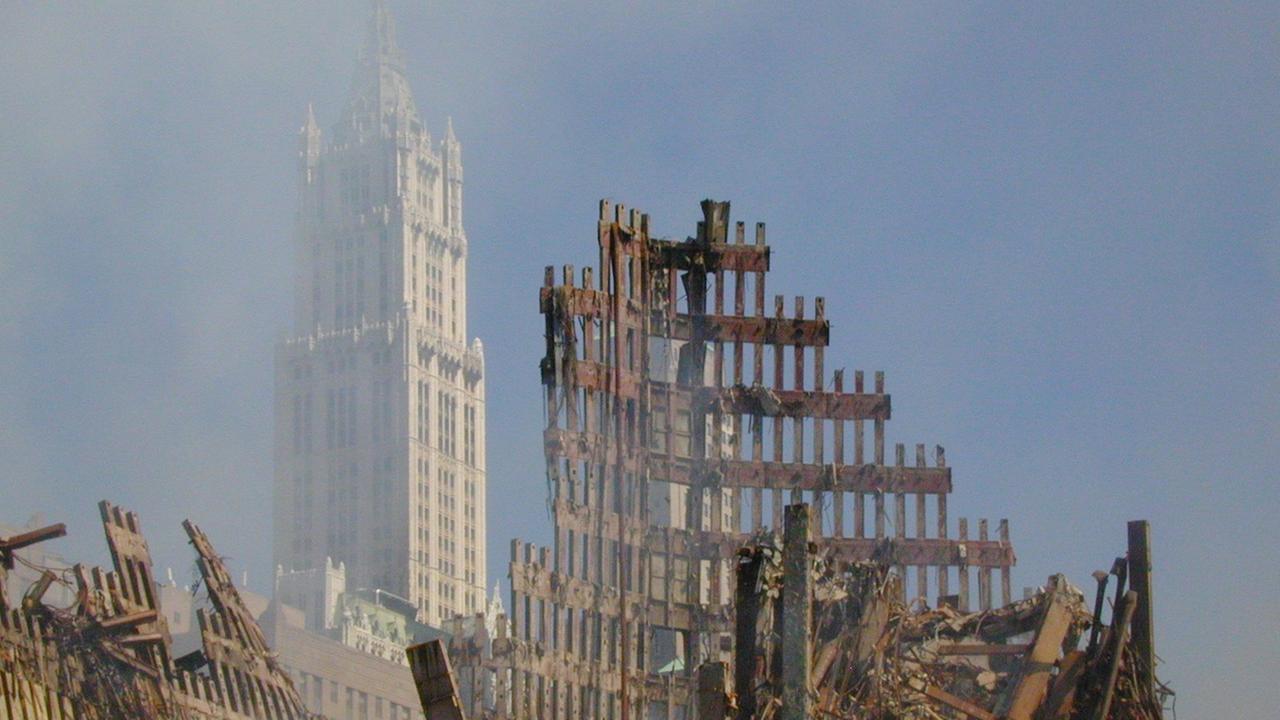 Hinter den Trümmern des World Trade Centers ist das Woolworth Building in New York zu erkennen. Dahinter blauer Himmel.