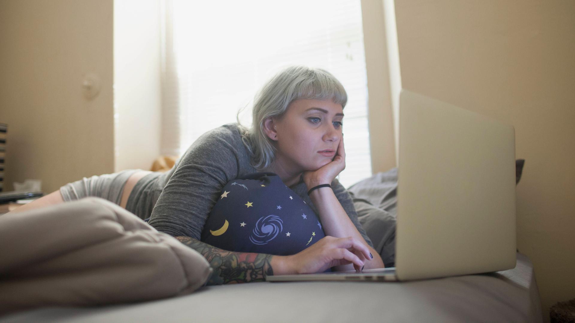 Eine Frau liegt auf dem Sofa und ist am Laptop beschäftigt.