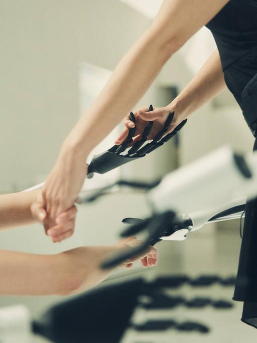 Roboterarme und menschliche Arme greifen ineinander.