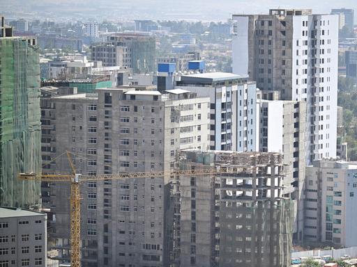 Ein Baukran steht vor teilweise fertig gestellten Hochhäusern.