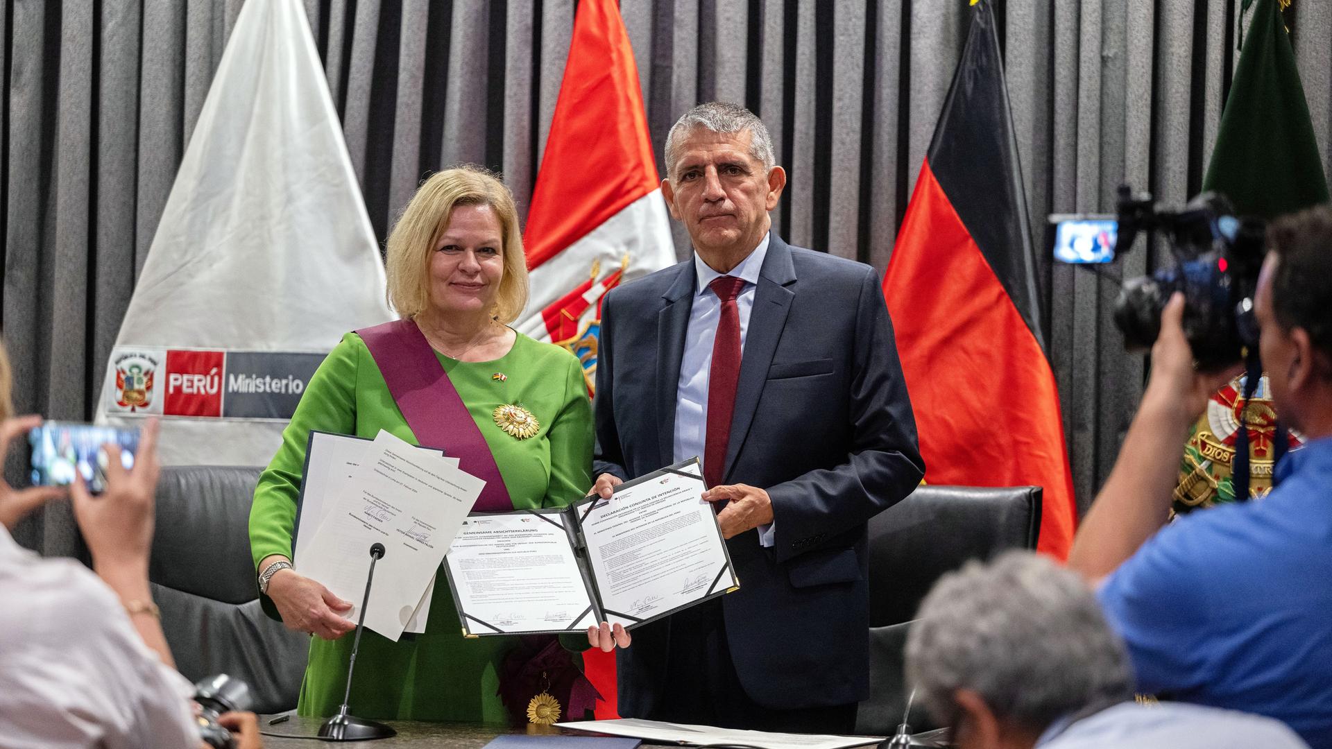 Die beiden stehen in einem Raum vor den Fahnen ihrer Staaten nebeneinander und halten die unterzeichneten Erklärungen in die Kameras. Vor ihnen Fotografen. Die beiden stehen in einem Raum vor den Fahnen ihrer Staaten nebeneinander und halten die unterzeichneten Erklärungen in die Kameras. Vor ihnen Fotografen.
