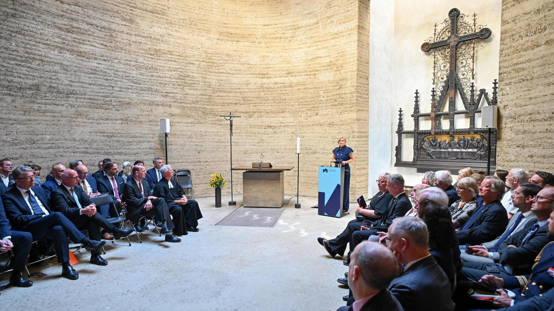 Bundestagspräsidentin Julia Glöckner hält eine Rede in der Kapelle der Versöhnung in Berlin. Viele Zuhörer sitzen links und rechts in Stuhlreihen. 