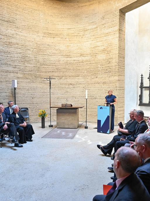 Bundestagspräsidentin Julia Klöckner hält eine Rede in der Kapelle der Versöhnung in Berlin. Viele Zuhörer sitzen links und rechts in Stuhlreihen. 