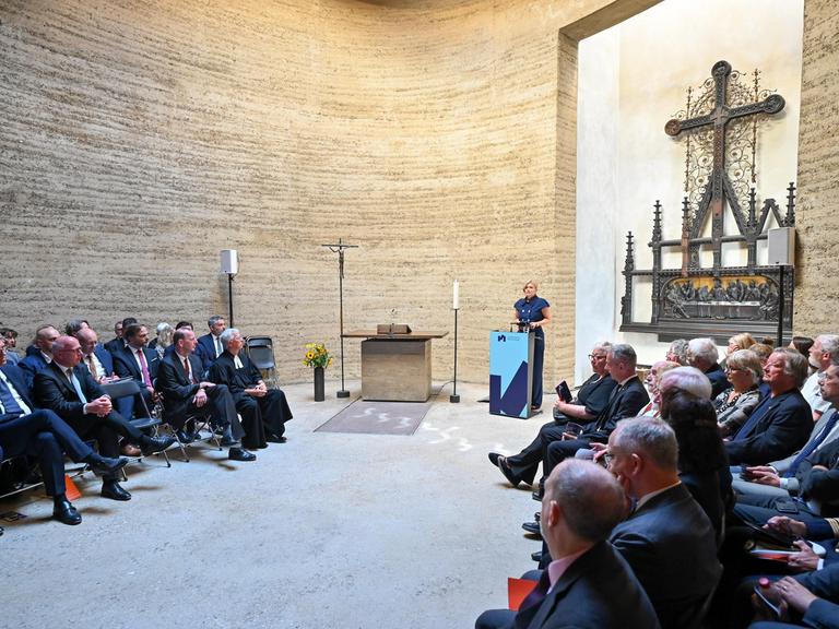 Bundestagspräsidentin Julia Klöckner hält eine Rede in der Kapelle der Versöhnung in Berlin. Viele Zuhörer sitzen links und rechts in Stuhlreihen. 