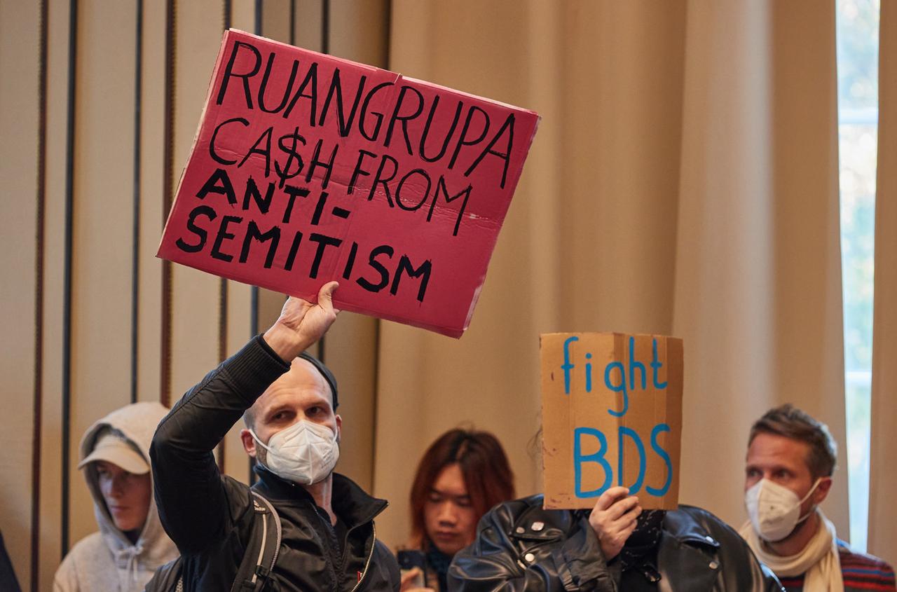 Protestierende halten in der Aula der Hochschule für bildende Künste Hamburg (HfbK) Transparente mit der Aufschrift "Ruangrupa C$sh From Antisemitism" und "Fight BDS" hoch.