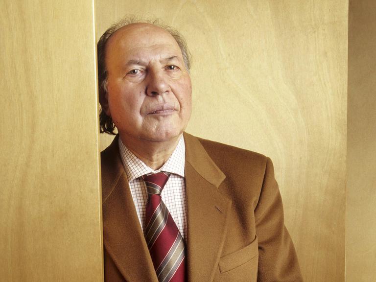 Imre Kertesz lehnt an einer holzvertäfelten Wand und blickt ernst in die Kamera Imre Kertesz lehnt an einer holzvertäfelten Wand und blickt ernst in die Kamera