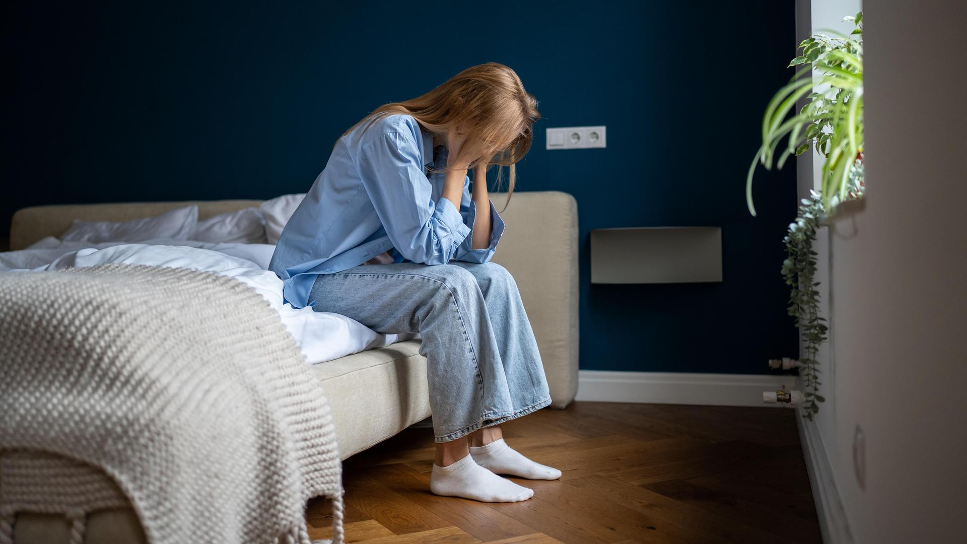 Eine einsame Frau sitzt auf einem Bett und hat die Hände im Gesicht vergraben.