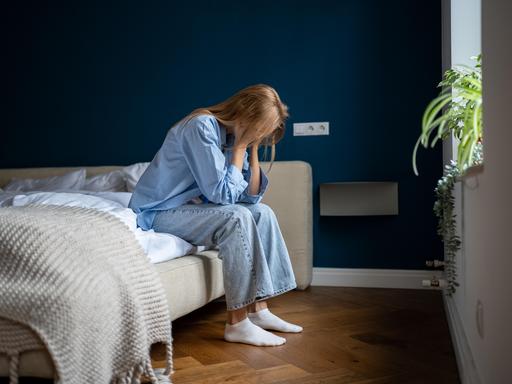 Eine einsame Frau sitzt auf einem Bett und hat die Hände im Gesicht vergraben.