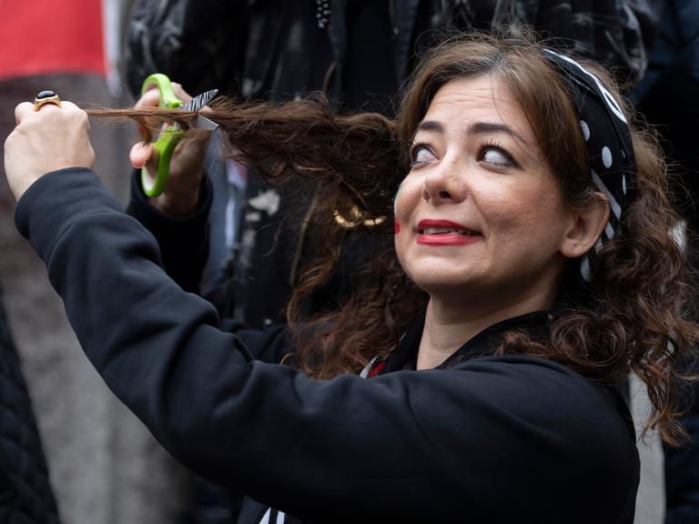 Eine Frau hält sich ein Schere an eine Strähne ihres Haares - Solidaritätsgeste für die Proteste im Iran auf einer Demo in Washington.