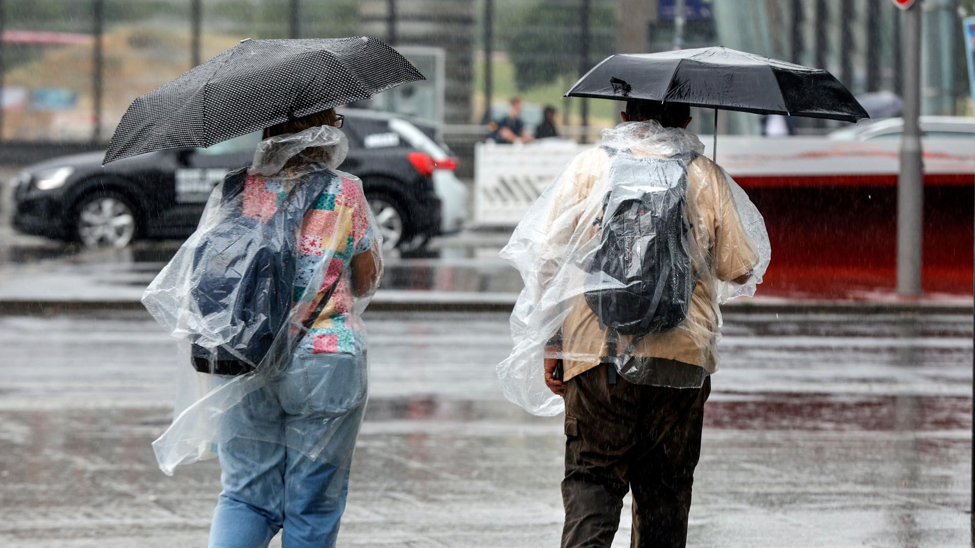 Füßgänger schützen sich mit Regencapes und Regenschirmen vor starkem Regenfall. 