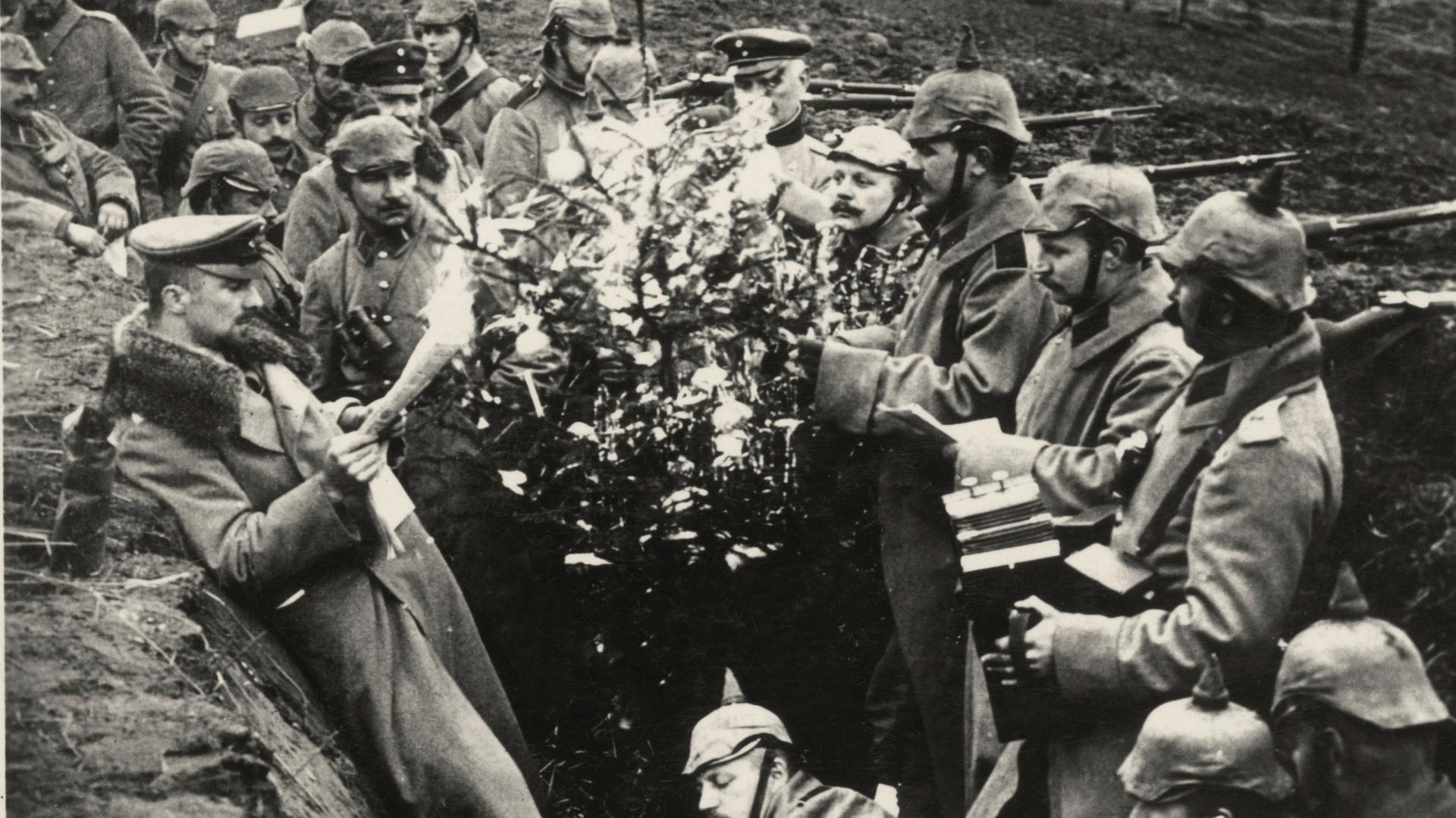 Deutsche Soldaten stehen zwischen einem Weihnachtsbaum in einem Schützengraben und singen