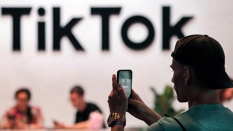 Ein Besucher der Messe Gamescom macht mit dem Smartphone ein Foto vom TikTok-Stand.