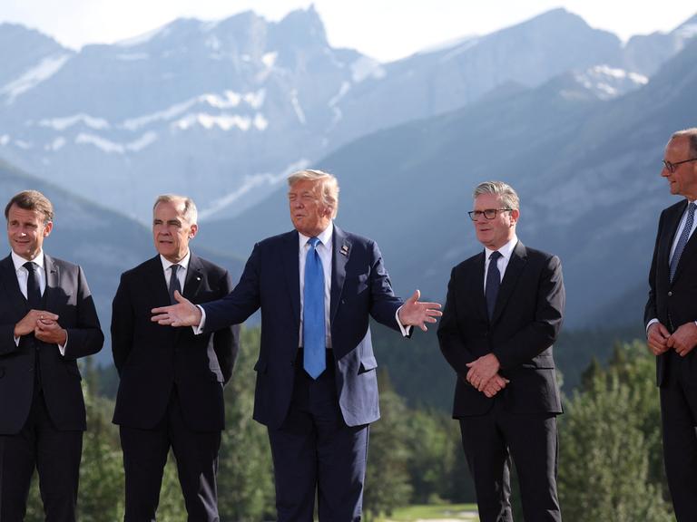 Emmanuel Macron, Mark Carney, Donald Trump, Keir Starmer und Friedrich Merz stehen vor den Bergen Alaskas beim G7-Gipfel zusammen