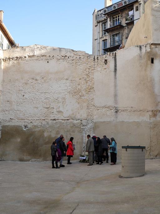 Menschen stehen bei einer Gedenkveranstaltung für die Opfer des Hauseinsturzes in Marseille in der Rue d'Aubagne an dem Platz, wo einmal zwei Häuser waren.