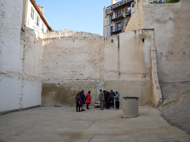 Menschen stehen bei einer Gedenkveranstaltung für die Opfer des Hauseinsturzes in Marseille in der Rue d'Aubagne an dem Platz, wo einmal zwei Häuser waren.