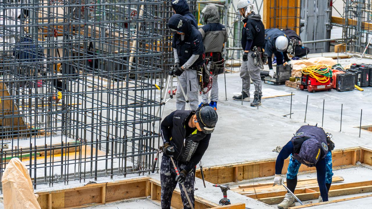 Mehrere Bauarbeiter arbeiten gemeinsam an einem modernen Rohbau mit Stahlbeton und Fundamenten. 