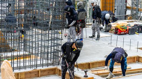 Mehrere Bauarbeiter arbeiten gemeinsam an einem modernen Rohbau mit Stahlbeton und Fundamenten. 