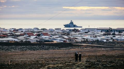 Ein Schiff der isländischen Küstenwache liegt vor Island im Meer. Auf dem Festland sind die Dächer von Häusern zu sehen. Ein Schiff der isländischen Küstenwache liegt vor Island im Meer. Auf dem Festland sind die Dächer von Häusern zu sehen.