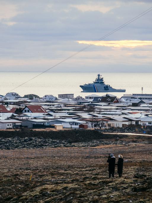 Ein Schiff der isländischen Küstenwache liegt vor Island im Meer. Auf dem Festland sind die Dächer von Häusern zu sehen.