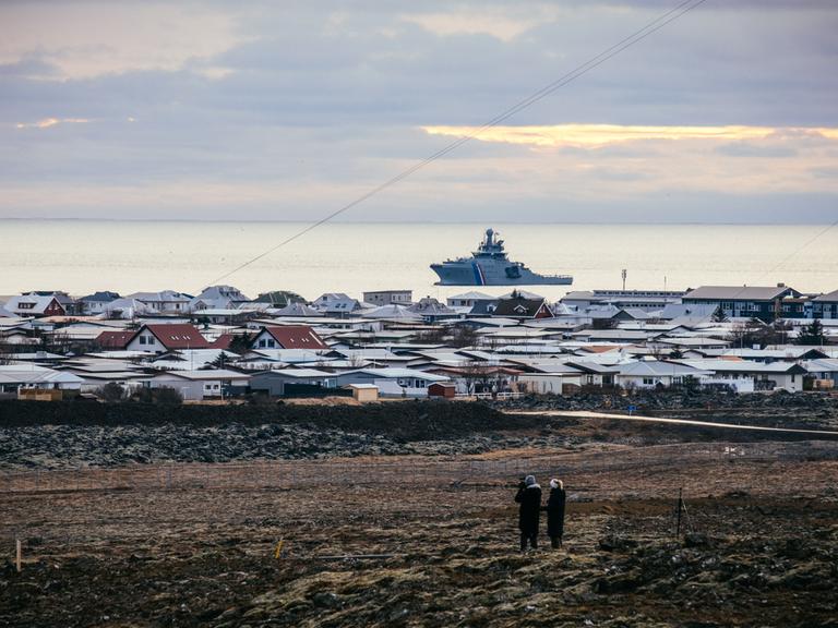 Ein Schiff der isländischen Küstenwache liegt vor Island im Meer. Auf dem Festland sind die Dächer von Häusern zu sehen.