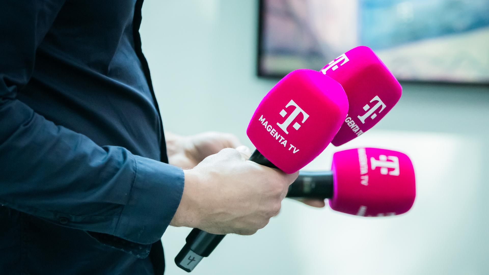 Ein Mann hält drei Mikrofone von Magenta TV in der Hand. Ein Mann hält drei Mikrofone von Magenta TV in der Hand.