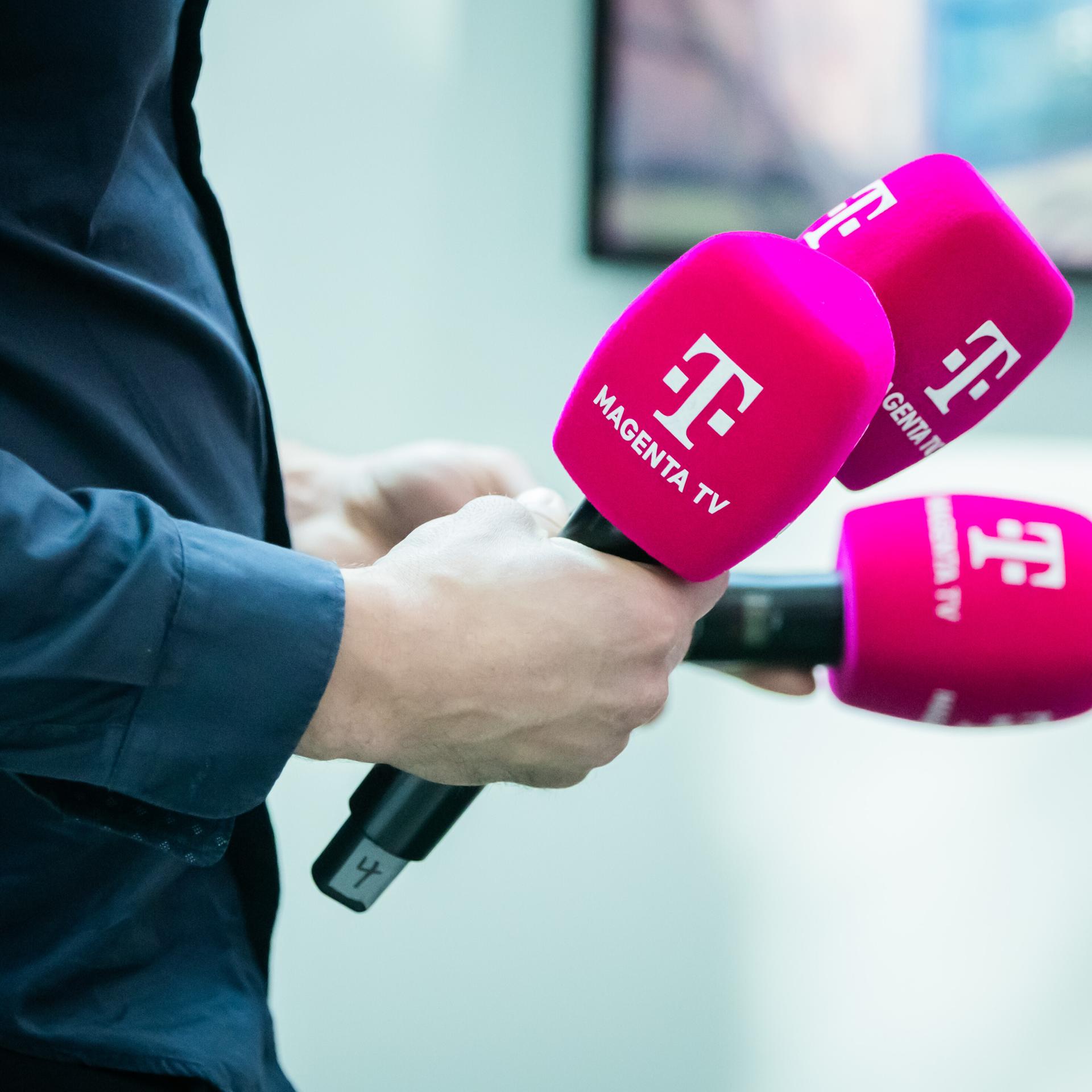 Ein Mann hält drei Mikrofone von Magenta TV in der Hand.
