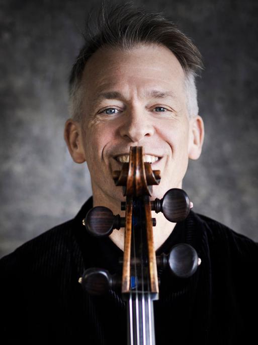 Alban Gerhardt lacht über die Schmecke seines Cellos hinweg, die er direkt vor sein Gesicht hält.