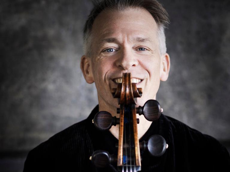Alban Gerhardt lacht über die Schmecke seines Cellos hinweg, die er direkt vor sein Gesicht hält.