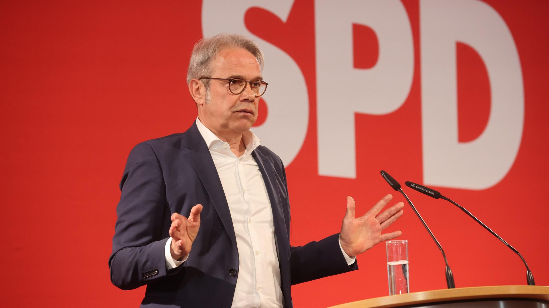 Georg Maier steht an einem Redepult und hält mit beiden Armen gestikulierend eine Rede. Im Hintergrund ist eine rote Wand mit einem großen weißen Logo der SPD zu sehen.